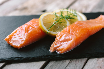 Red fish o salmon fillets on stone slate on wooden background. Fresh fish, lemon and dill for cooking ingredients. Concept of healthy eating. Omega-3. Close up.