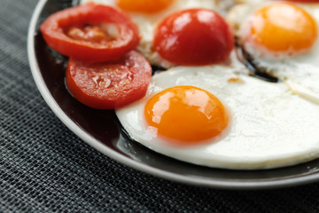 plate of fried eggs with tomato on dark background, top view