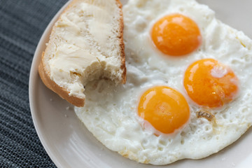 Three fried eggs and bread and butter on a plate.