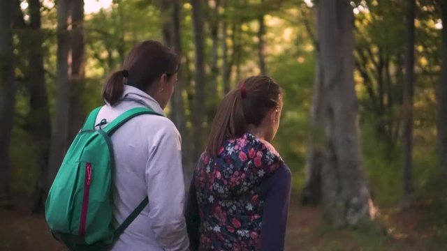 Mother and young teenage daughter talk while hiking together through forest.