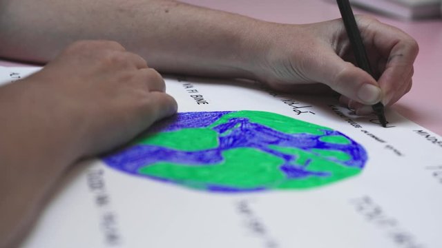 Close up on hands writing all will be ok in many languages around a colorful earth. Zoom in