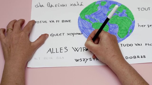 Zoom out on hands writing all will be ok in all languages around a colored earth