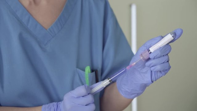 Nurse preparing Coronavirus Vaccine. Camera zoon in on blue liquid.
