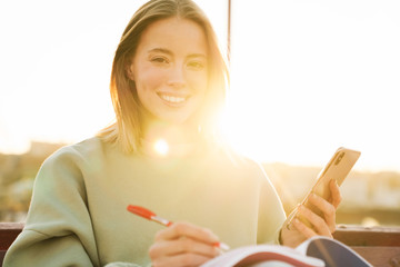 Portrait of woman using cellphone and studying with exercise books