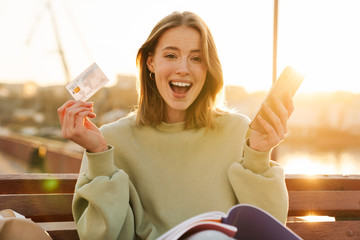 Portrait of excited young woman holding cellphone and credit card
