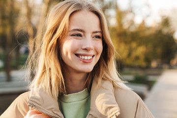 Portrait of young blonde woman smiling and looking aside while walking