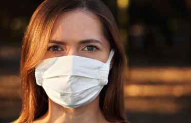 Young woman wearing white cotton virus mouth nose mask, nice bokeh, park afternoon sun, in...