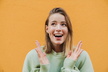 Portrait of excited blonde woman smiling with throwing up hands