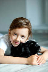 Portrait of happy smiling little girl hugging black guinea pig.