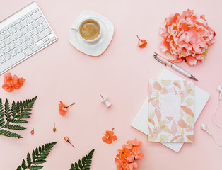Top view Freelancer home office desk. Blogger workspace with coffee, keyboard, flowers and stationery on pink background