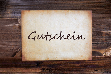 Obraz na płótnie Canvas Old Grungy Paper With German Text Gutschein Means Voucher. Wooden Background