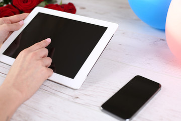Hand hold tablet and touching on workspace on table with phone and roses