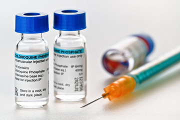 Chloroquine phosphate drug in small injection bottles with blue caps, orange green syringe near, closeup detail (own label design with dummy data - not real product) Potential coronavirus cure concept