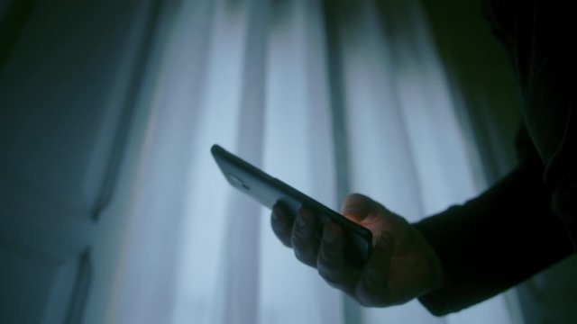 Man using a 5G smartphone while texting with his thumb at home at night detail shot