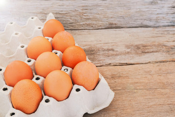 Close-up view of raw chicken eggs in egg box on wooden background.