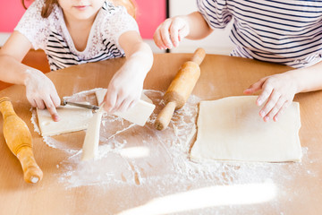 Obraz na płótnie Canvas A girl and little sister are cooking pastries in the kitchen at the table, flour and rolling pin, cooking with children, delicious food, junk food, carbohydrates, breakfast, croissants
