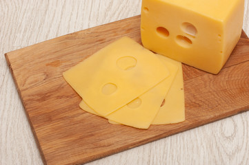 Piece of cheese and sliced cheese on a wooden board