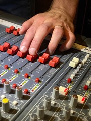 Hand adjusts faders on mixing desk