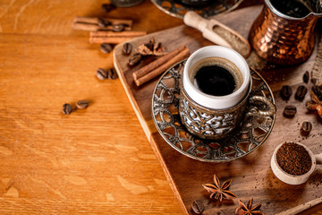 Detail of a coffee cup surrounded by coffee beans and spices on a natrual wood background