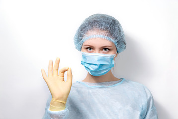 A young doctor in a medical uniform says that everything will be OK. The masked doctor gestures with his hands that everything will be all right.