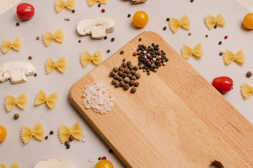 Uncooked pasta, tomatoes, mushroom slices and spices on a beige background, top view, close-up. Cooking, fettuccine, yellow and red cherries.