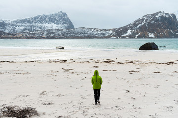 Woman walking along an empty ocean beach Kvalvika and looking at the mountains. Fjord in Norway....
