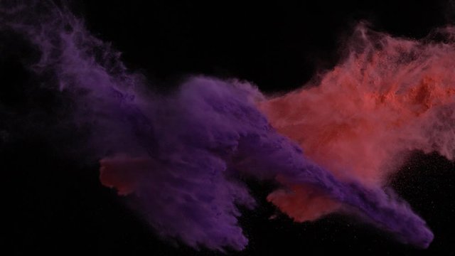 In real slow motion footage against a black background, a cup of purple powder and red powder are thrown from opposite sides at equal heights and combine in the air. Side Shot.