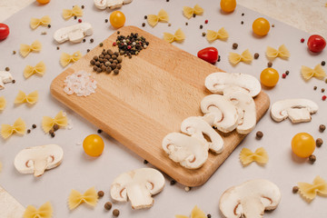 Uncooked pasta, tomatoes, mushroom slices and spices on a beige background, top view, close-up. Cooking, fettuccine, yellow and red cherries.