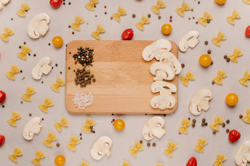 Fototapeta na wymiar Uncooked pasta, tomatoes, mushroom slices and spices on a beige background, top view, close-up. Cooking, fettuccine, yellow and red cherries.