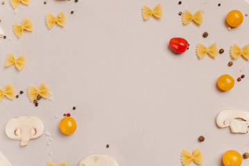 Uncooked pasta, tomatoes, mushroom slices and spices on a beige background, top view, close-up. Cooking, fettuccine, yellow and red cherries.