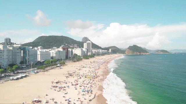 Drone flies over Copacabana beach in Rio de Janeiro with people on the sand enjoying leisure time