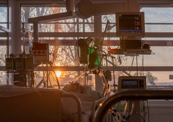 Patient connected to medical ventilator, and to monitor in ICU in hospital,  the windows sun rises.