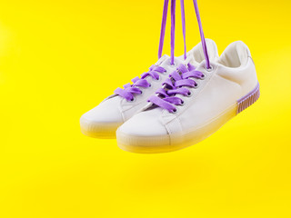 White sneakers with purple laces on yellow background. Modern minimal fashion art trendy bold color still life