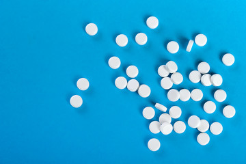 A lot of white pills scattered on a blue background. Top view, free space.