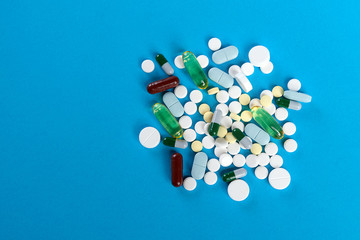 Tablets and capsules scattered on a blue background. Top view, close-up.