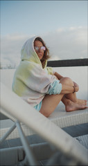 young woman relaxing on the beach. Beautiful girl dressed in sports clothes sitting and relaxing. She is dressed in colored hoodie, eyes glasses. 