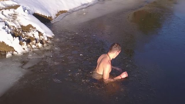 Young man under water in partially frozen mountain lake rises to the surface and turns to exit. Danger of hypothermia and risk of cold water in winter. Polar plunge, extreme Nordic sport ice swimming.