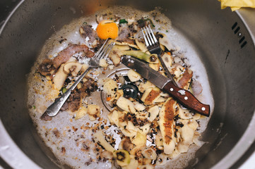 A metal sink in which there are two forks, a knife with a wooden handle and potato peel. The...