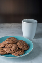 Delicious crunchy homemade chocolate cookies on a plate with coffee mug, marble table with dark background. Breakfast concept