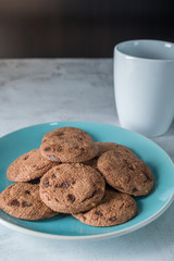 Delicious crunchy homemade chocolate cookies on a plate with coffee mug, marble table with dark background. Breakfast concept