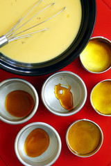 Tin molds with caramel syrup beside a Leche flan batter