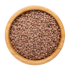 Dried brown lentils in wooden bowl isolated on white. Top view.
