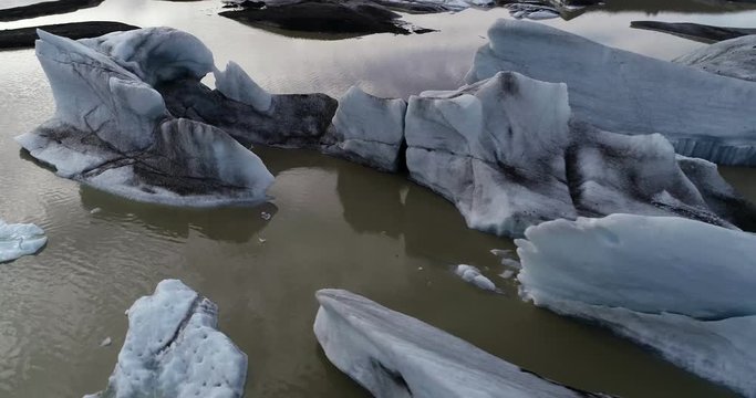 Aerial drone video flying over roughly broken hunks of glacier ice floating in a lagoon