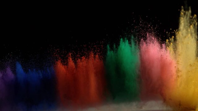 In real slow motion footage against a black background, purple, blue, orange, green, pink and yellow powder bursts into frame from below like a fountain. Side shot.