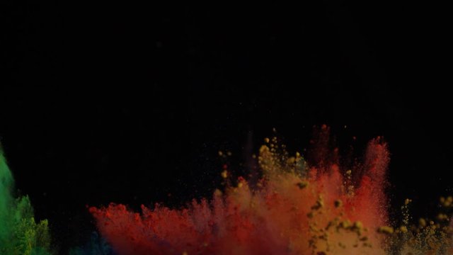 In real slow motion footage against a black background,  Green, red, yellow and orange powder explodes sporadically into frame and mixes in the air. Side shot