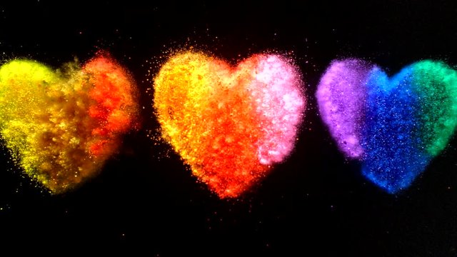 In real slow motion footage, three heart shaped clumps of powder, two with warm colors and one with cool colors burst brilliantly and simultaneously like fireworks. Top Shot.