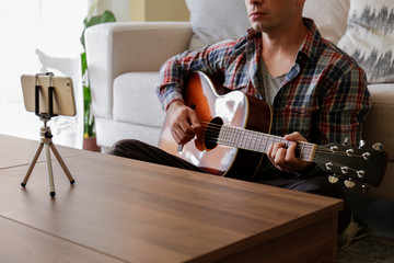 Music college hipster student in checkered shirt practicing acoustic guitar exercise, reading notes from laptop. Man taking an online musical courses at home during quarantine. Background, close up