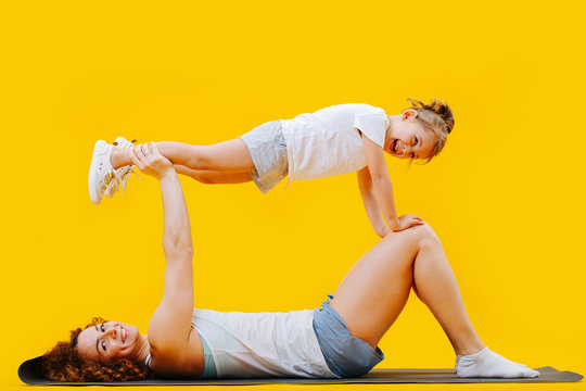 Girl doing plank in the air standing on mom's hands and knees over yellow