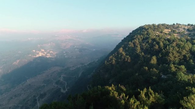 Aerial flight toward pine trees over cliff tilt down to high elevation panoramic view