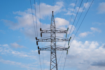 Power pole and lines with transformers and street light, bright blue sky with clouds